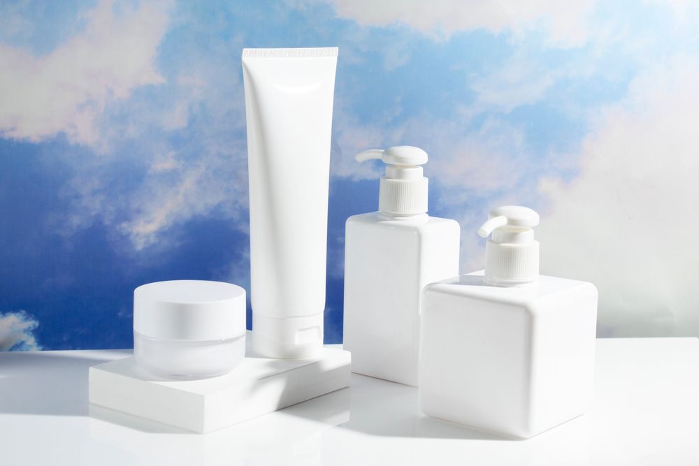 Various white minimalist packaging components including a collapsible tube, lotion pump, and a jar