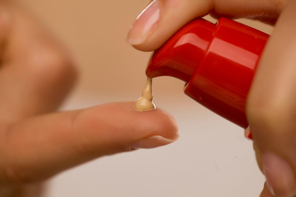 A hand pumping out foundation with a red treatment pump